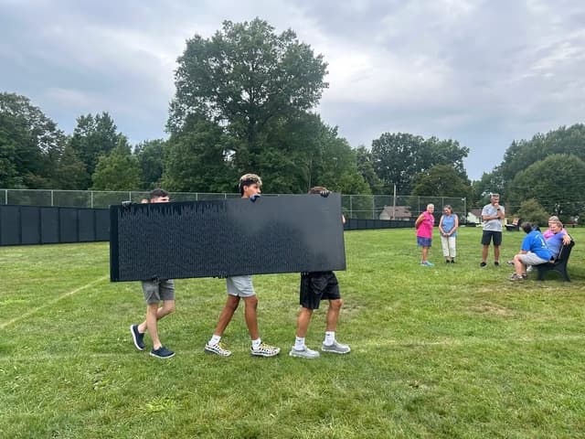 Volunteers carry a panel of the Wall across the field at Blue Tip Park
