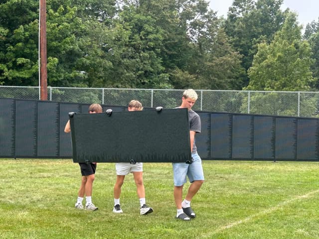 Three volunteers carry a panel across the grass