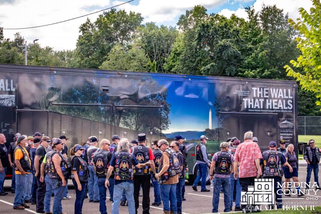 Motorcycle riders in vests gather beside the exhibit trailer before the escort