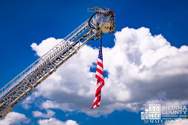 A fire department ladder truck flies a large American flag above the route