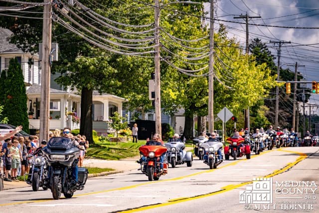 The motorcycle escort moves down a street lined with neighbors