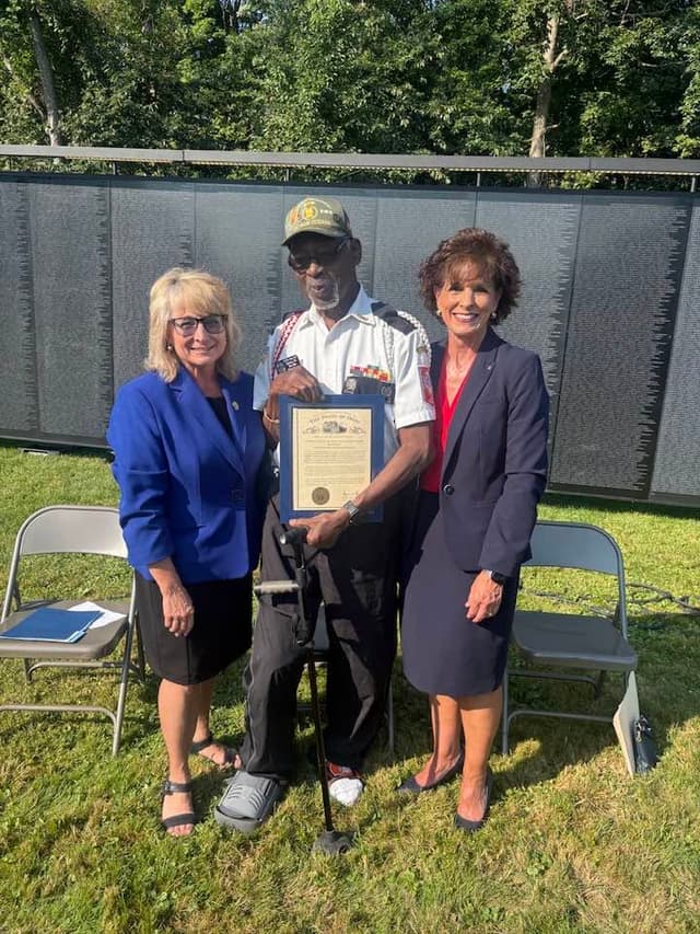 A veteran receives a framed recognition beside the Wall
