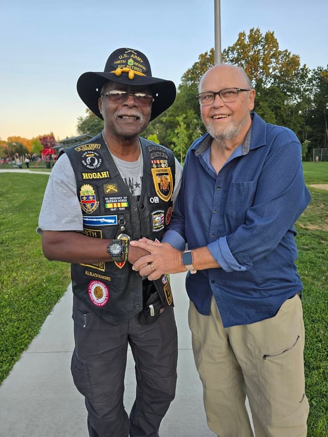 Two veterans stand arm in arm beside the Wall
